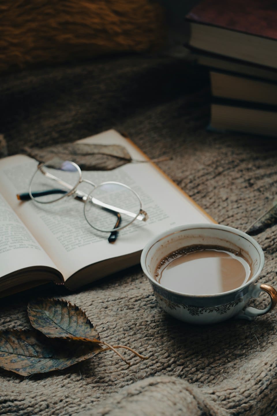 Open book, glasses, and coffee on a knitted blanket.