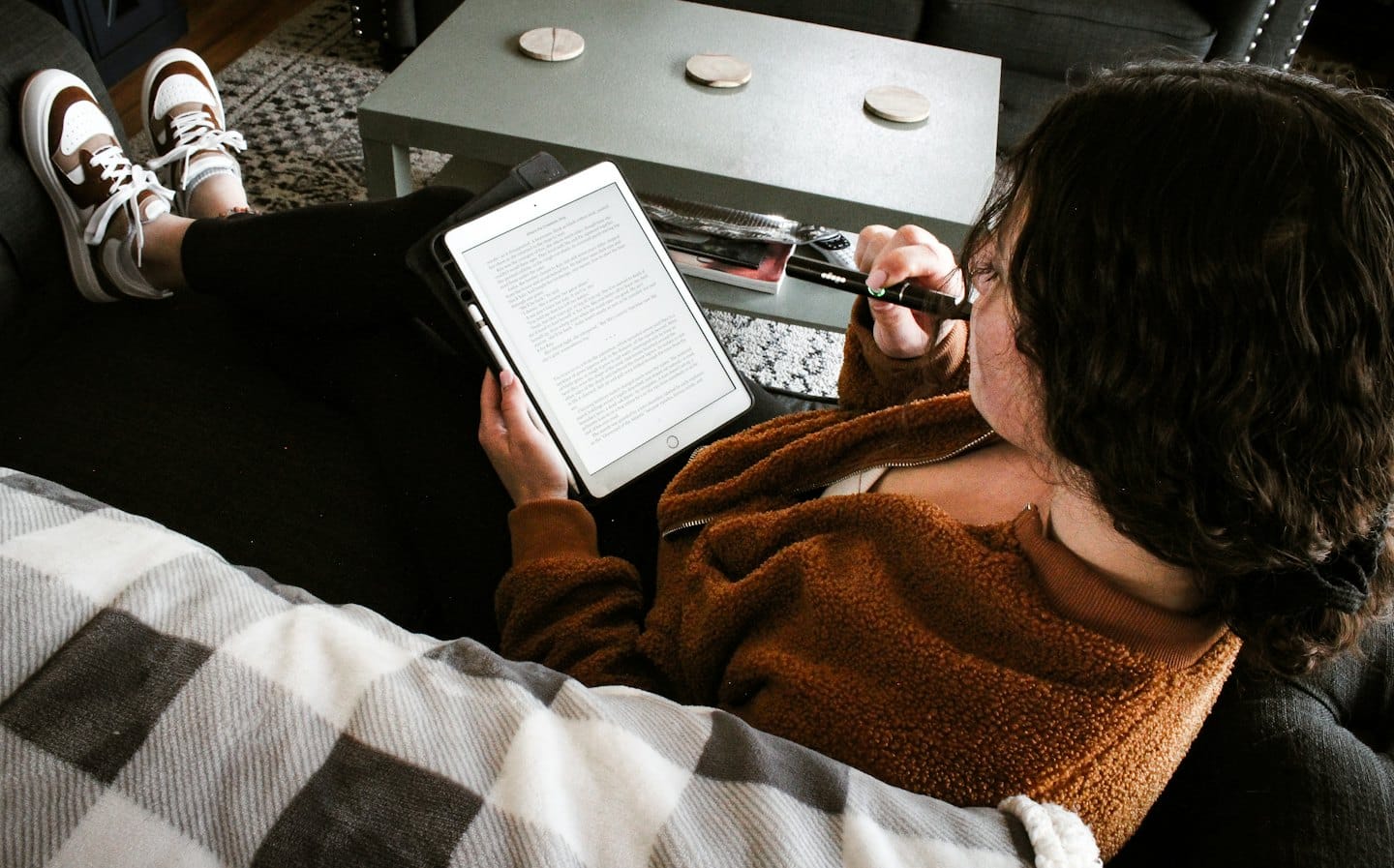 Person in brown jacket reading on tablet on couch.