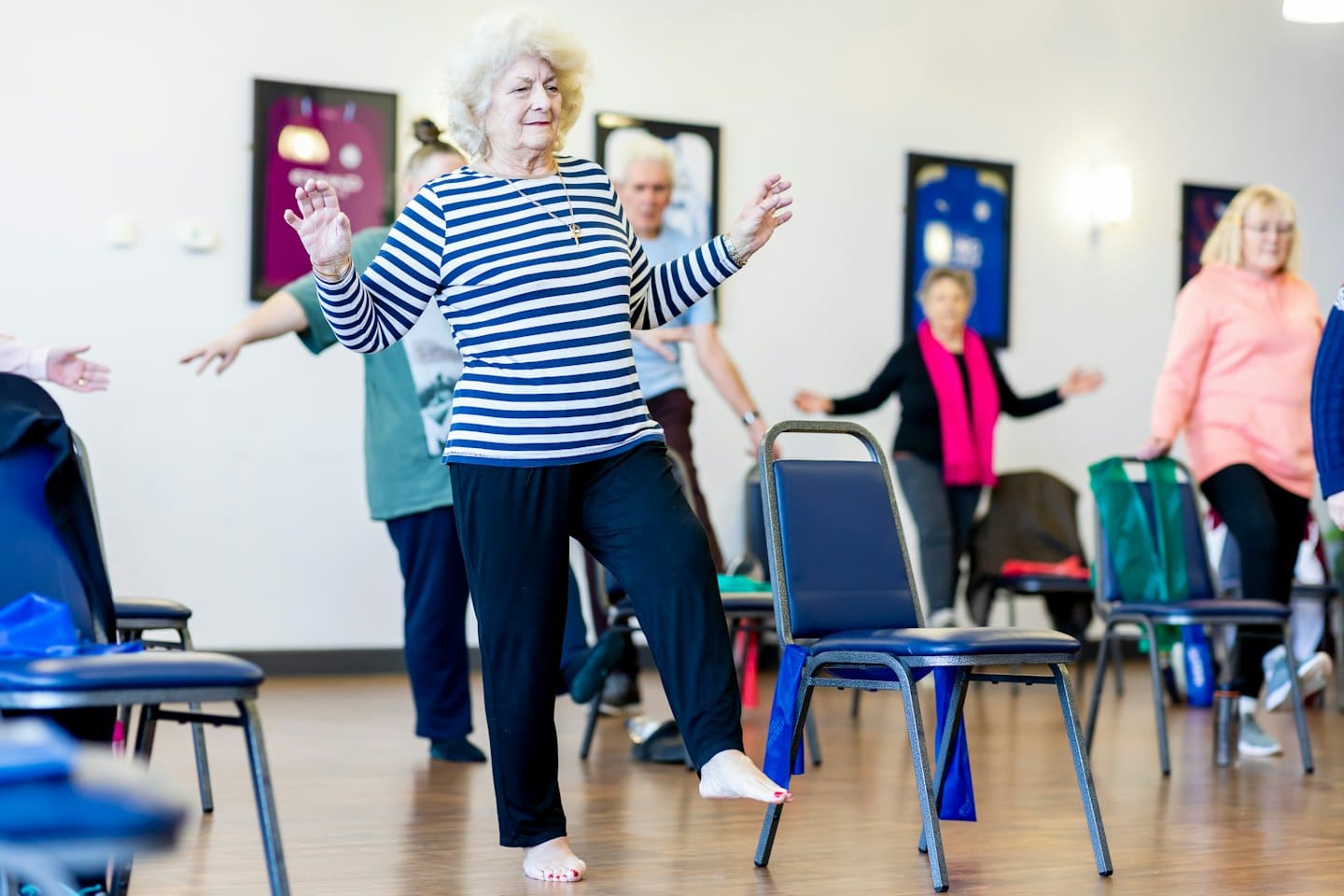 Elderly adults practice chair-supported balance exercises indoors.