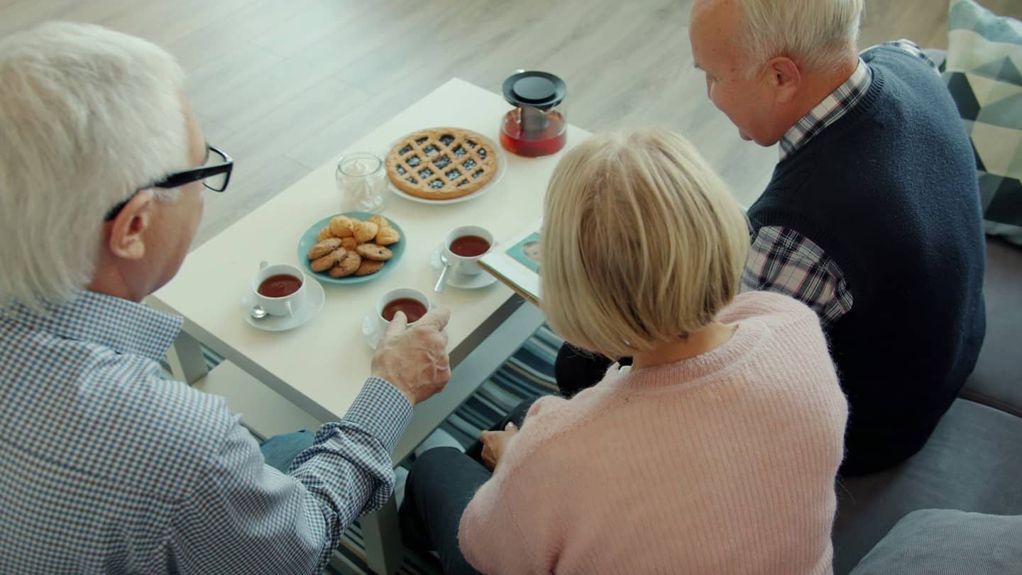 Three people enjoying tea and snacks around a coffee table.