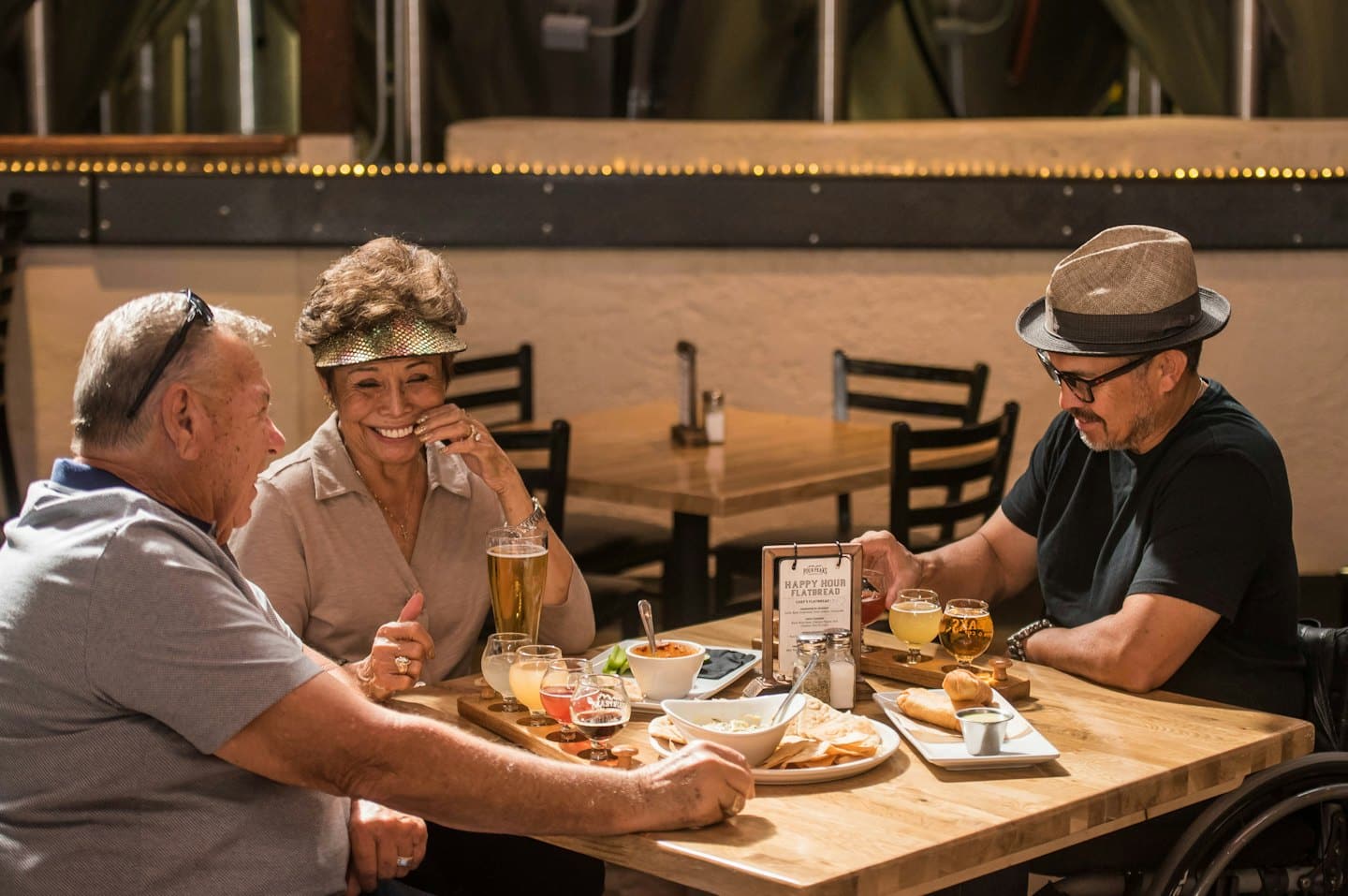 Three adults socializing with drinks and food at brewery tables.